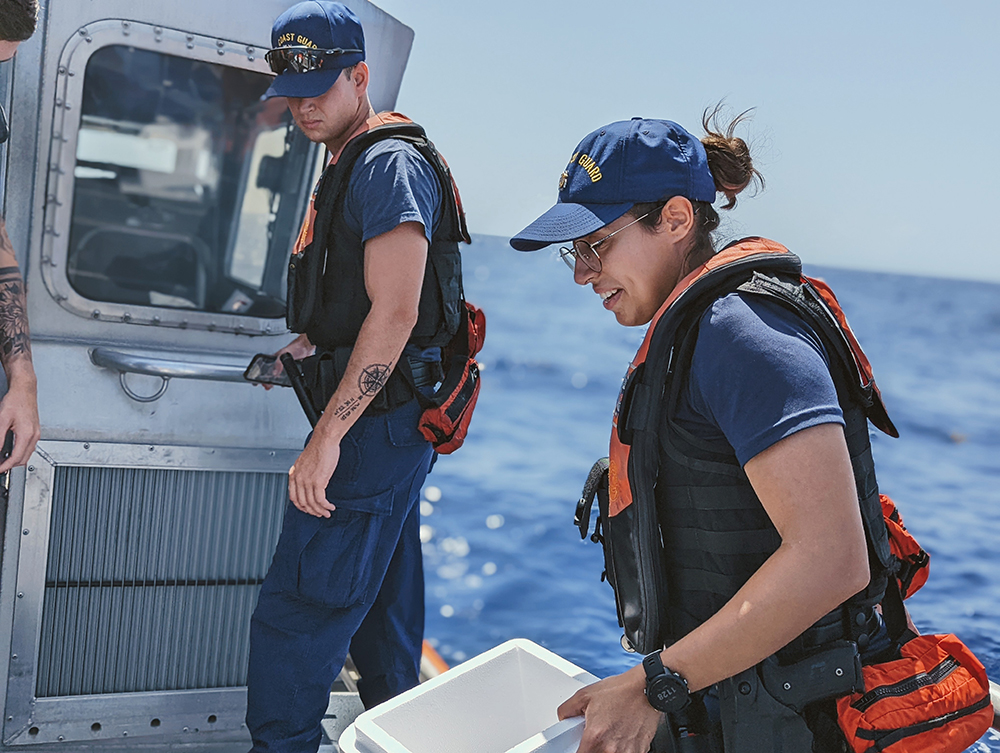 Two Coastguard members assist Turtle Transort aboard the deck of a marine vessel